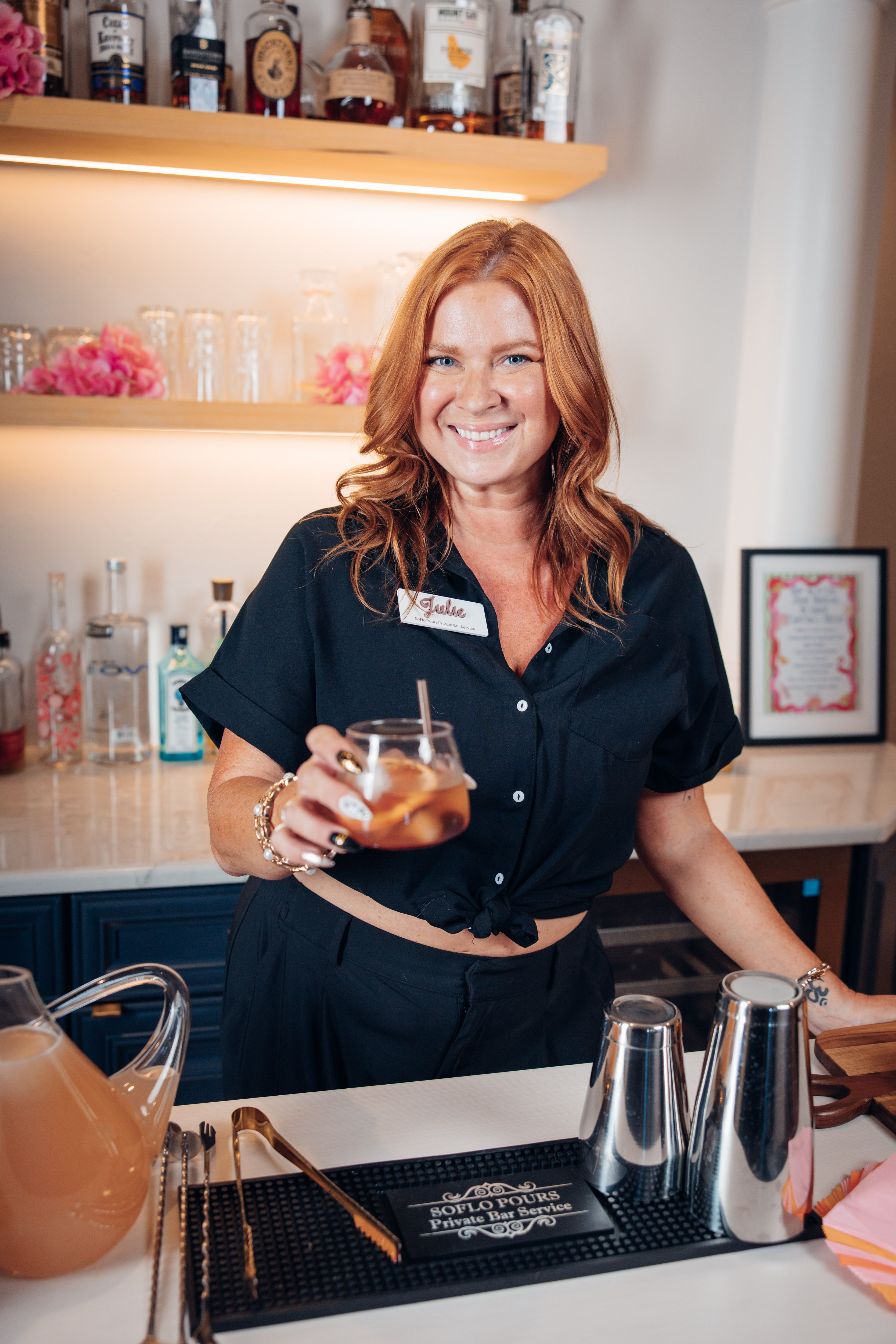 Naples Florida Bartender Smiling bartender holding a cocktail in a bar with bottles and glassware in the background